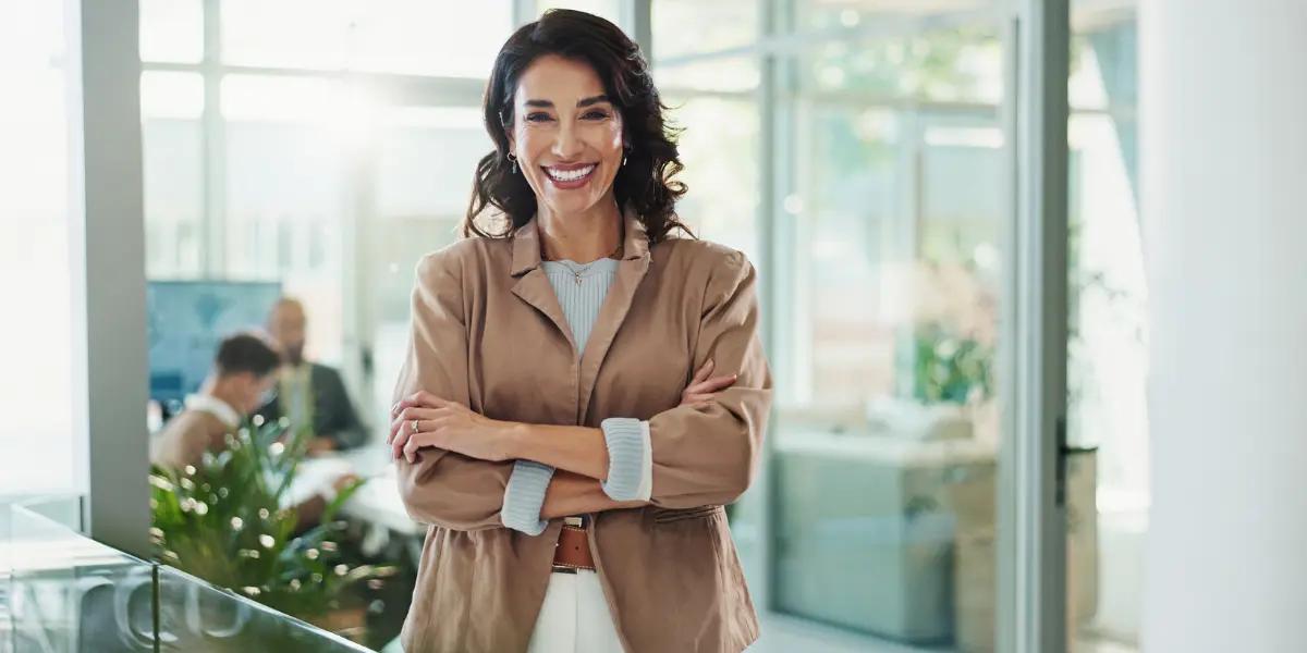 Corretora de imóveis parada em frente da fachada da sua imobiliária.